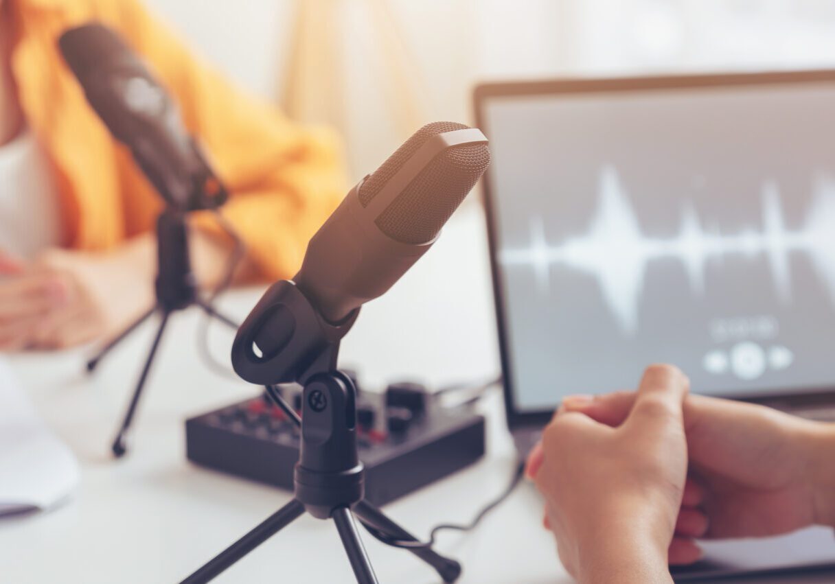 Podcast microphone setup with audio wave on computer screen.