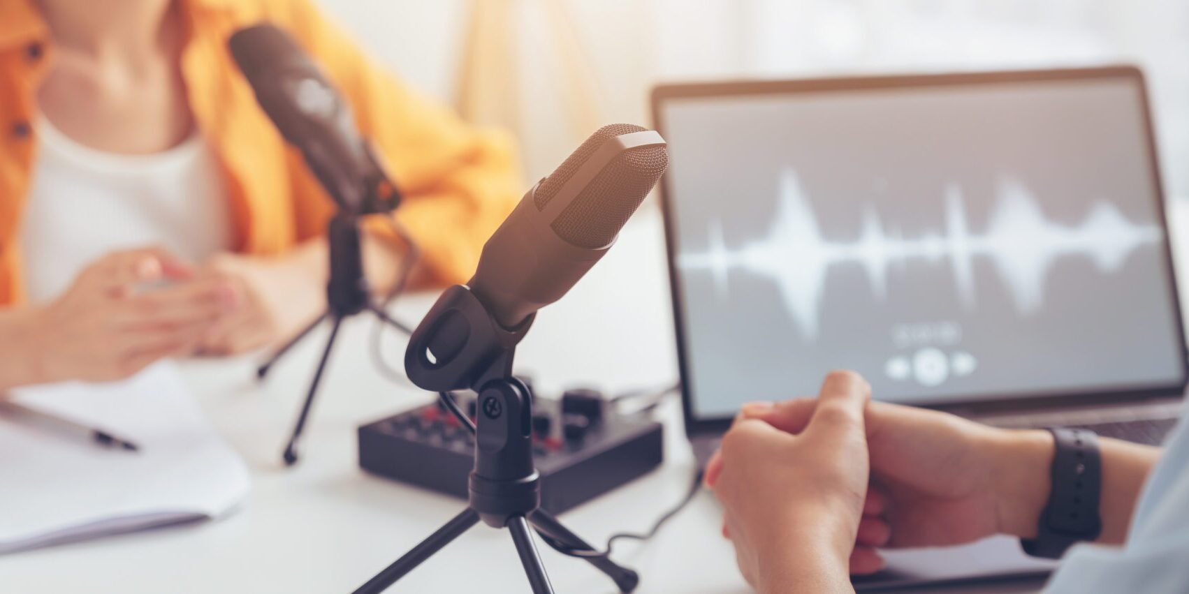 Podcast microphone setup with audio wave on computer screen.